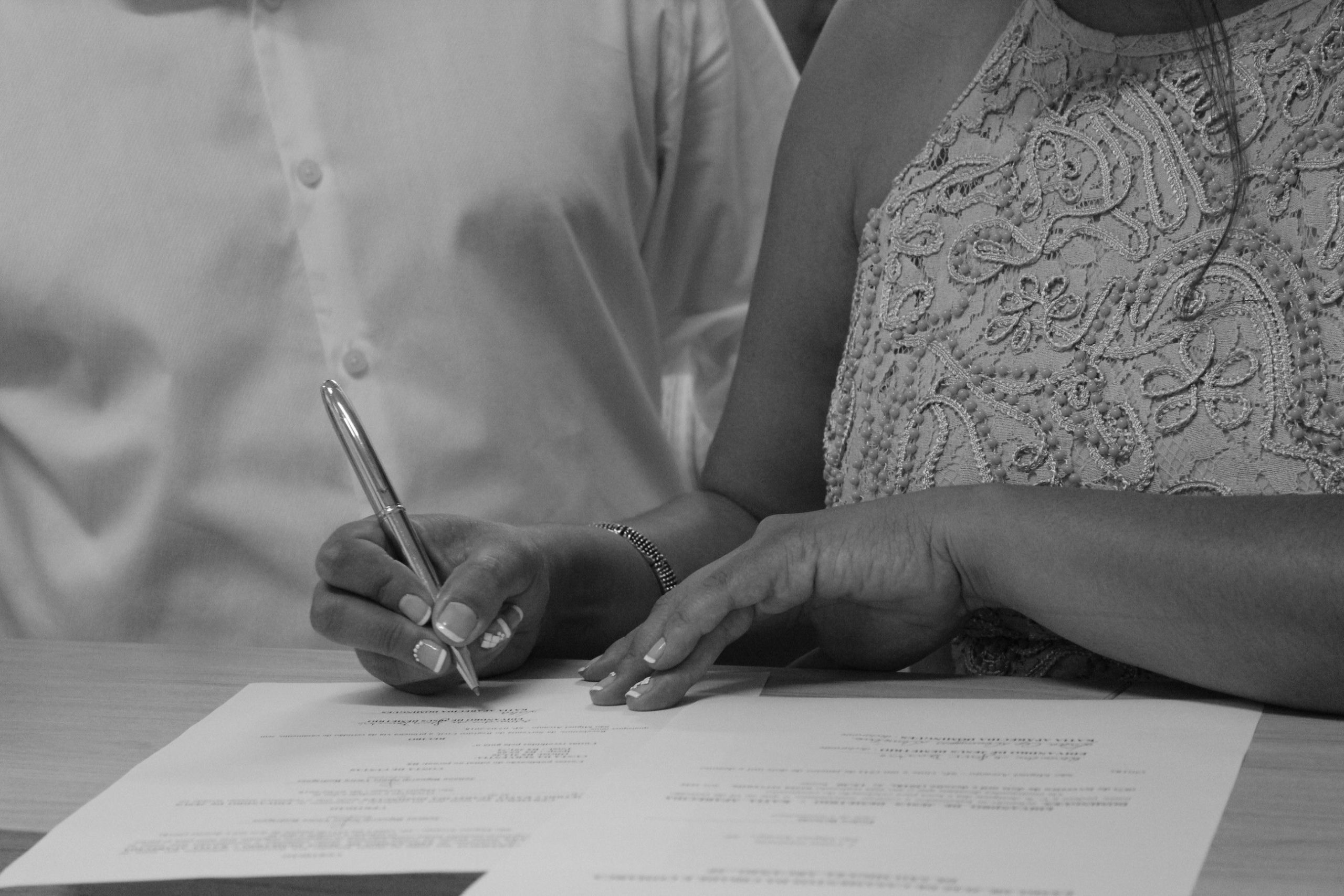 Mains de couple signant documents en noir blanc